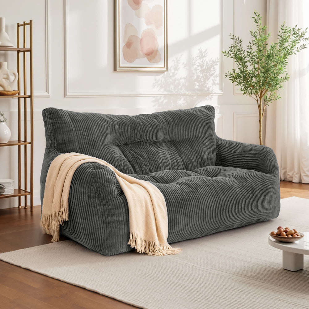 A dark gray corduroy loveseat sofa in a bright, modern living room setting, styled with a cream throw blanket draped over one arm.