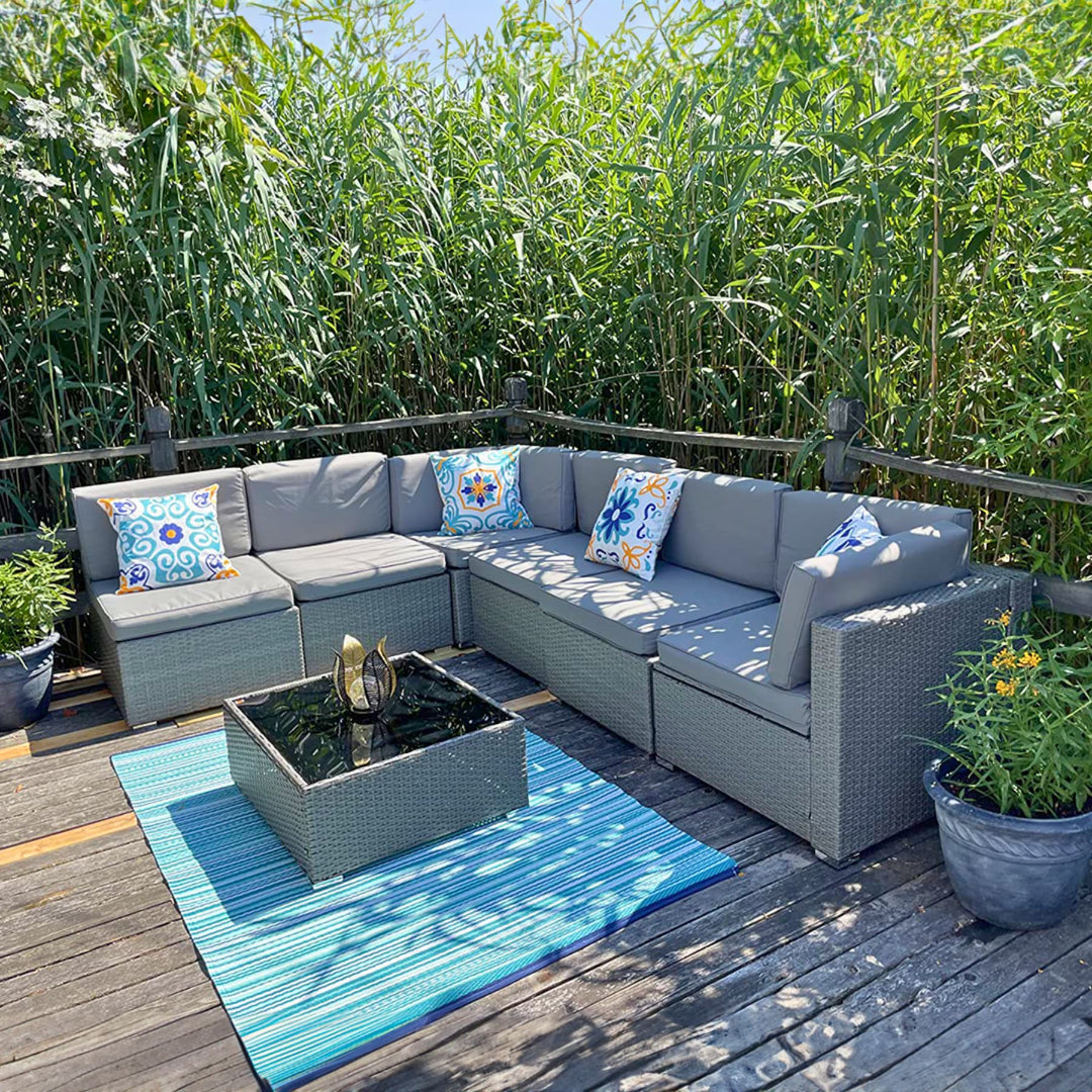 Outdoor patio with gray sectional sofa, blue rug, and decorative pillows on a wooden deck.
